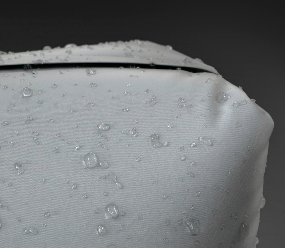 Macro of the bag's shell: water standing in beads on the woven nylon without soaking in, and the closed zip running across the top of the frame