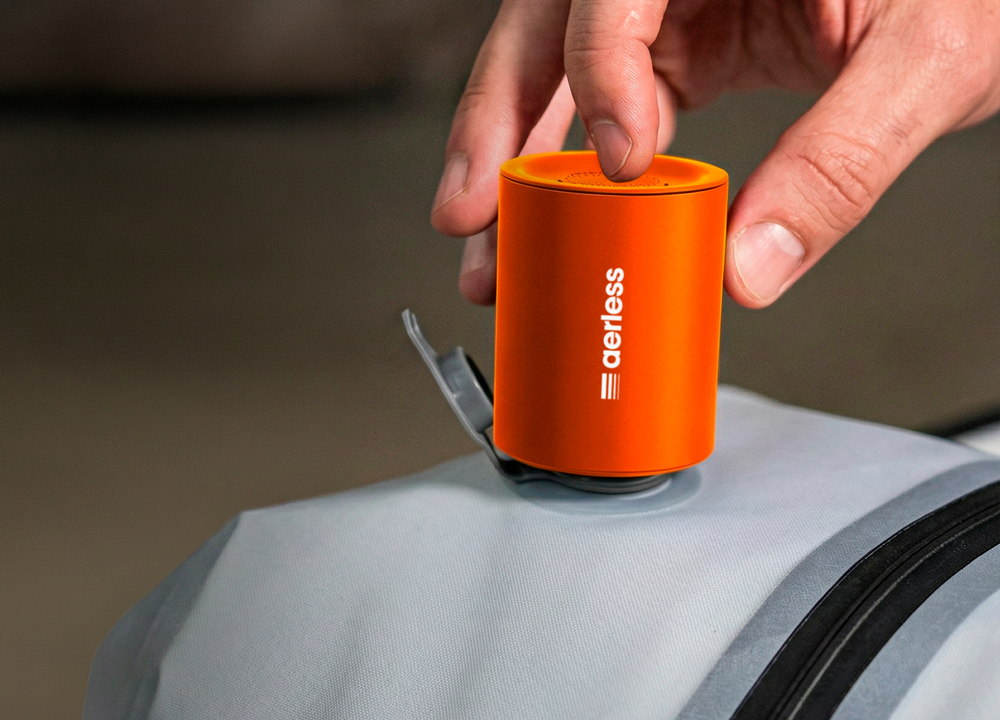A hand holding the small orange pump down onto the round valve port of a packed bag, the valve flap folded back out of the way